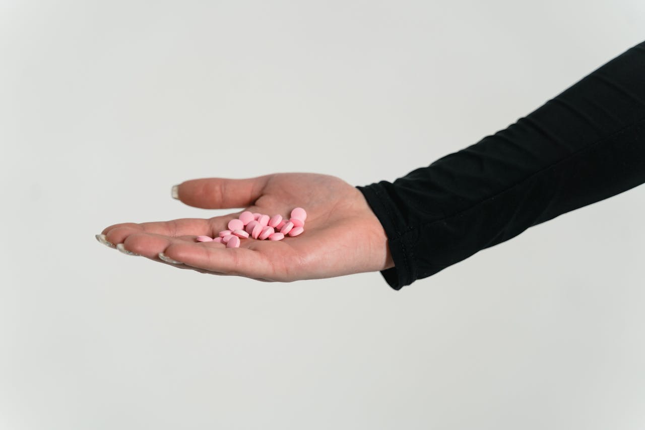 A close-up view of an outstretched hand holding pink pills against a white background.
